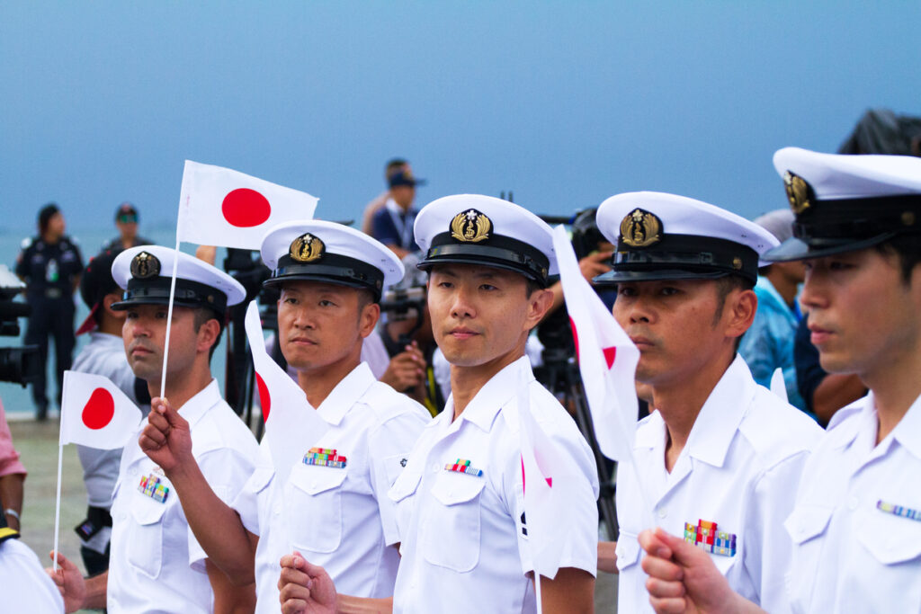 Row of walking japanese navy officers captured during asean fleet parade in Pattaya. Some officers are carrying small japanese flag.