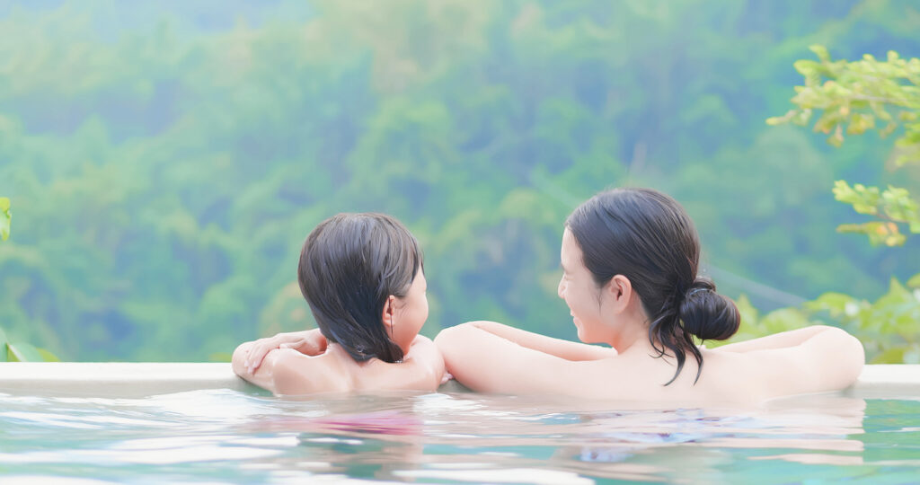 rear view of asian mother and daughter enjoy outdoor hot spring