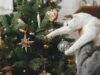 Cute cat together with woman decorating stylish christmas tree with vintage baubles. Pet and winter holidays. Woman in cozy sweater hugging adorable kitty in festive room. Merry Christmas!