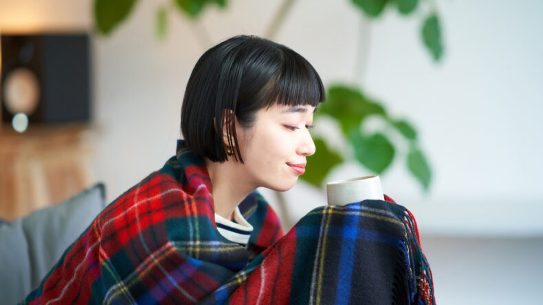 Young woman wearing a blanket and holding a mug
