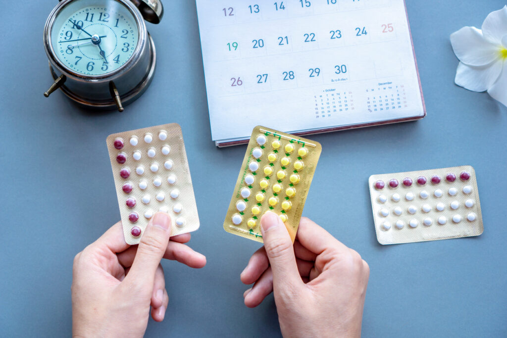 Woman Hand Choosing Oral Contraceptive Pills, With Calendar And Clock On Background