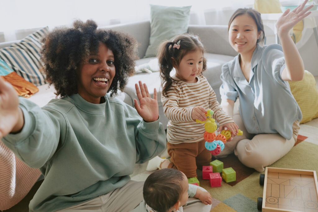 African American blogger smiling and waving while taking selfie with her Asian friend and her daughter during playing, bloggers son interested in bricks Moms Friends in Japan