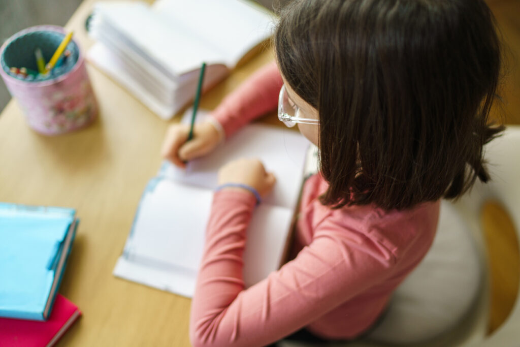 Above view of girl whit brown hair writing homework