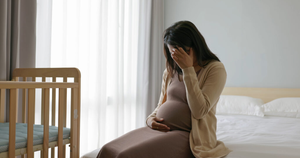 asian pregnant woman touch her belly sit on bed side - she is feeling depression kind of sad crying in room