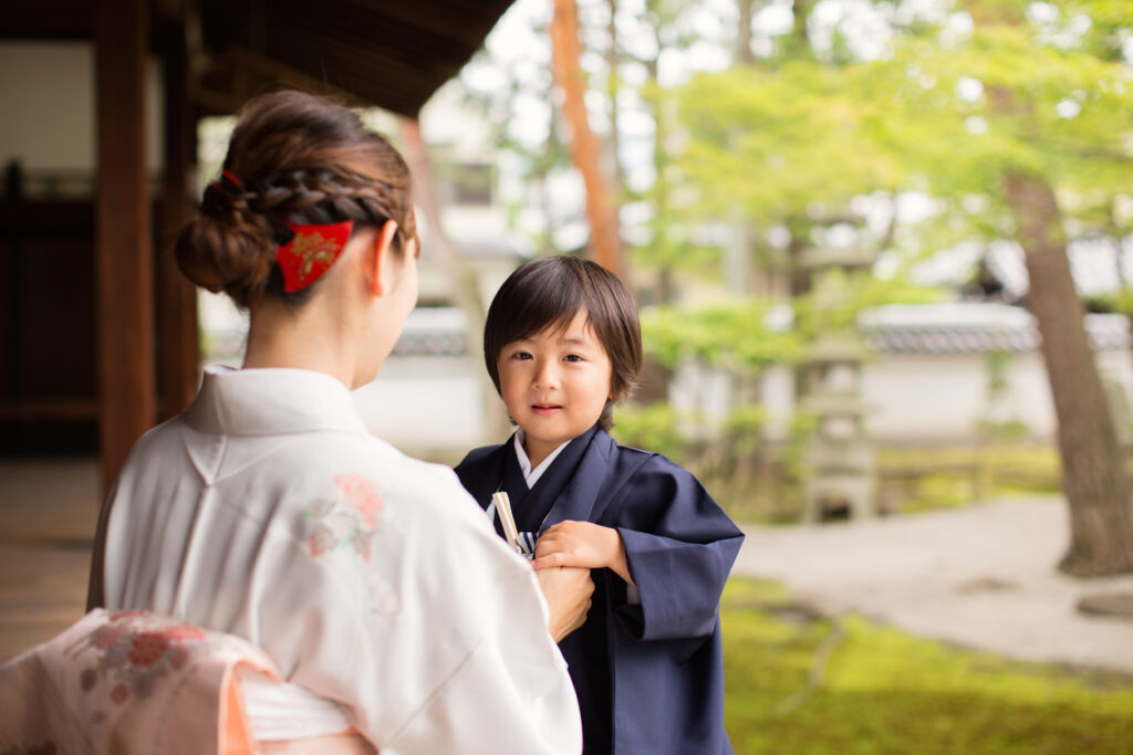 A young Japanese boy and his mother wear traditional kimono dress while celebrating shichi-go-san. He is looking at the camera while his mother straightens his robe. Shichigosan is a coming of age rite for 5 year old boys. They are at the Chion-ji Temple in Kyoto Japan.
